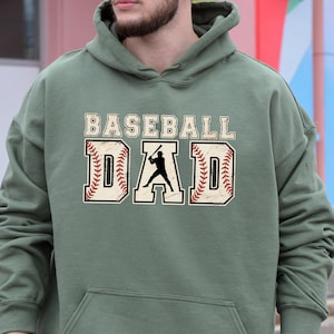 May include: A green hooded sweatshirt with the text "Baseball Dad" in white with a baseball player silhouette and red stitching around the text.