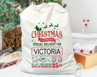 May include: A white Christmas gift bag with a red and green design. The bag has the text "Christmas Express" and "Special Delivery for Victoria". It also says "Do Not Open Before December 25th".