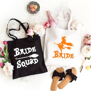 May include: Two black and white tote bags with Halloween-themed bridal party designs. One bag says "Bride Squad" with a white broom and the other says "Bride" with an orange witch silhouette.