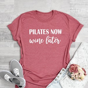 K&ouml;nnte beinhalten: Korallenrosa T-Shirt mit dem Text "Pilates Now Wine Later" in wei&szlig;en Buchstaben.