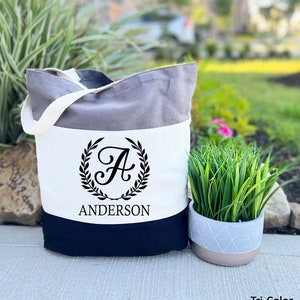 May include: A tri-color tote bag with a gray, white, and black design. The bag features a black monogram with the letter "A" surrounded by a wreath and the name "Anderson" printed below.