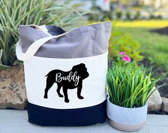May include: A tri-color tote bag with a grey, white, and black design. The bag features a black silhouette of a bulldog with the name "Buddy" written in white text.