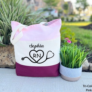May include: A pink, white, and burgundy tote bag with the name "Sophia" and a heart with "RN" inside, along with a stethoscope, printed on the front.