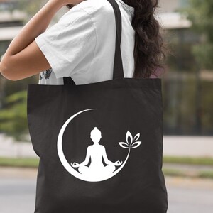 May include: Black canvas tote bag with a white silhouette of a person meditating in a crescent moon with a leaf design.