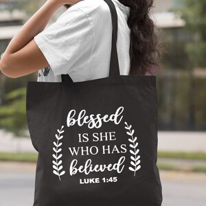 May include: Black canvas tote bag with white text that reads "blessed is she who has believed" and "LUKE 1:45".
