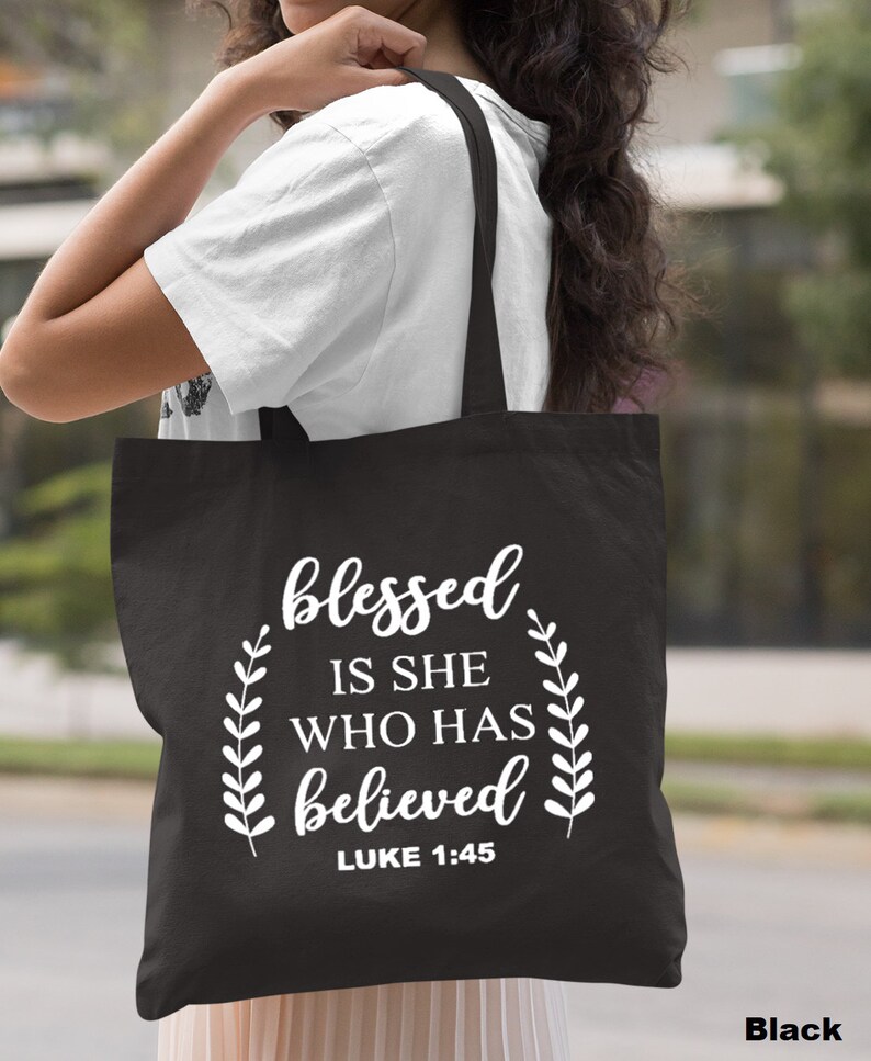 May include: Black canvas tote bag with white text that reads "blessed is she who has believed" and "LUKE 1:45".