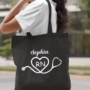 May include: Black tote bag with white text and a graphic of a stethoscope and heart with the letters RN inside. The text on the bag reads "Sophia".