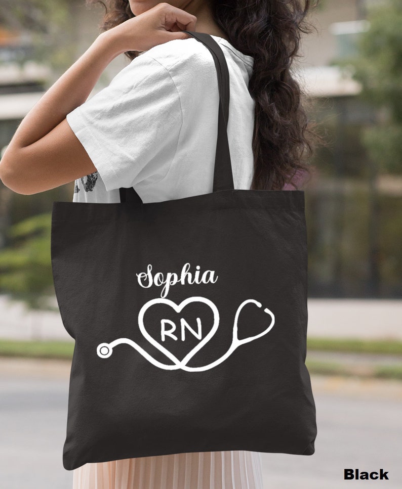 May include: Black tote bag with white text and a graphic of a stethoscope and heart with the letters RN inside. The text on the bag reads "Sophia".