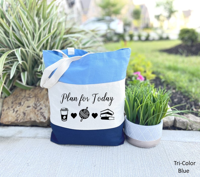 May include: A blue and white tote bag with the text "Plan for Today" and icons of a coffee cup, yarn ball, and books. The bag has a white canvas base with a blue top and a dark blue bottom.