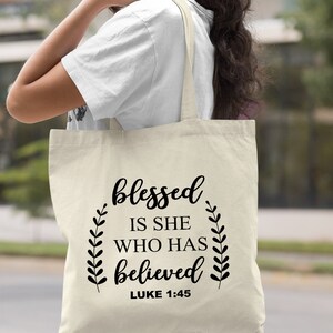 May include: A natural canvas tote bag with black text that reads "blessed is she who has believed Luke 1:45".