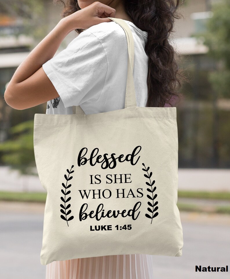 May include: A natural canvas tote bag with black text that reads "blessed is she who has believed Luke 1:45".