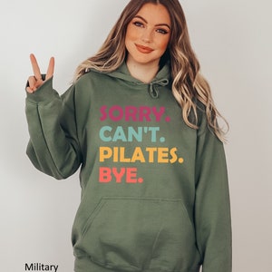 May include: A green hooded sweatshirt with the text "SORRY. CAN'T. PILATES. BYE." printed in colorful letters.