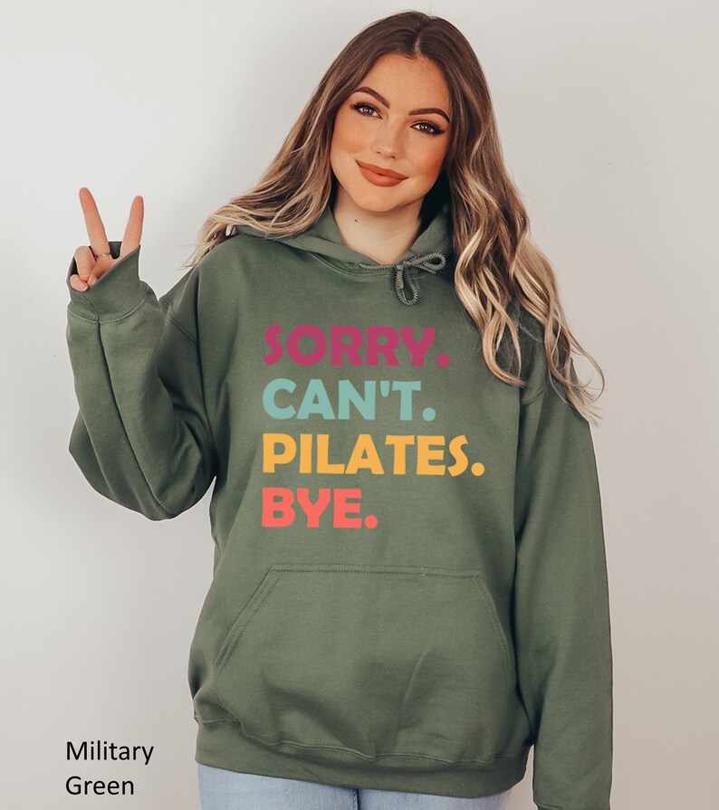 May include: A green hooded sweatshirt with the text "SORRY. CAN'T. PILATES. BYE." printed in colorful letters.