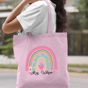 May include: Light pink tote bag with a rainbow, pencils, an apple, and hearts. The text "Mrs. Wilson" is printed on the bag.