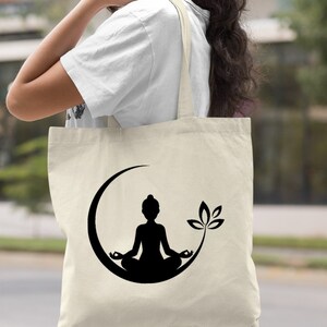 May include: A natural canvas tote bag with a black silhouette of a person meditating in a crescent moon with a lotus flower. The text "Natural" is printed on the bottom right corner of the image.
