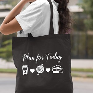 May include: Black tote bag with white text that reads "Plan for Today" and icons of a coffee cup, yarn, and books.