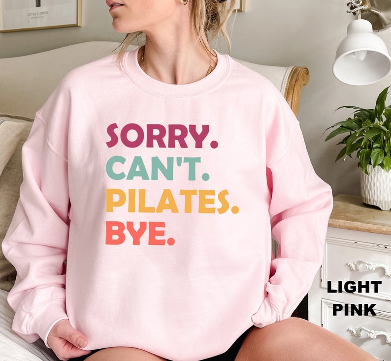 May include: A light pink sweatshirt with the text "SORRY. CAN'T. PILATES. BYE." in colorful letters.