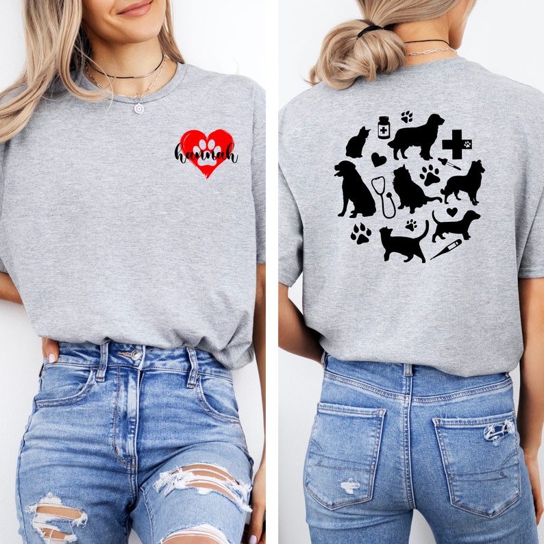 Op de afbeelding: Een grijs T-shirt met een rood hart en het woord "hannah" op de voorkant. De achterkant van het shirt heeft een ontwerp met verschillende dieren, waaronder honden, katten en een stethoscoop.