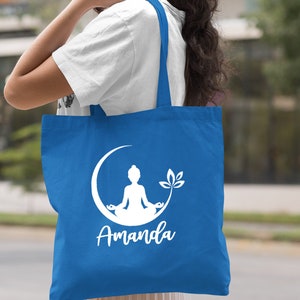 May include: A royal blue tote bag with white handles. The bag features a white silhouette of a person meditating on a crescent moon with a lotus flower. The name "Amanda" is printed below the image.