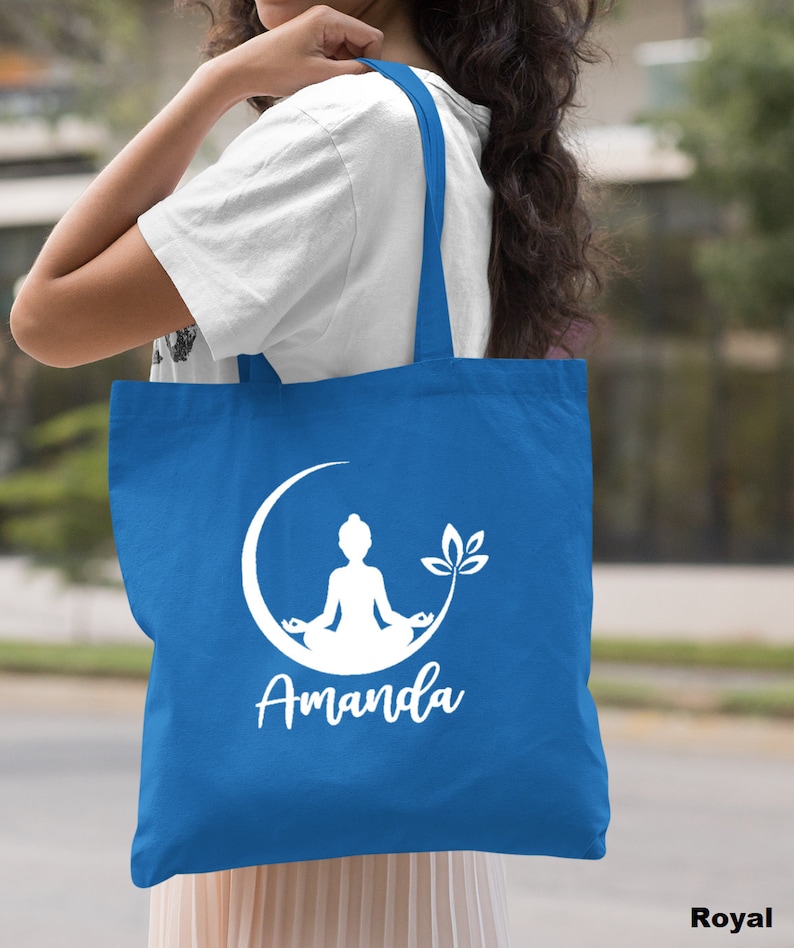May include: A royal blue tote bag with white handles. The bag features a white silhouette of a person meditating on a crescent moon with a lotus flower. The name "Amanda" is printed below the image.
