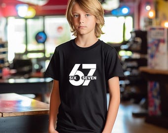 May include: Black t-shirt with the number "67" in white, with "SIX SEVEN" below. The shirt is worn by a person with blond hair, standing in front of a blurred background.