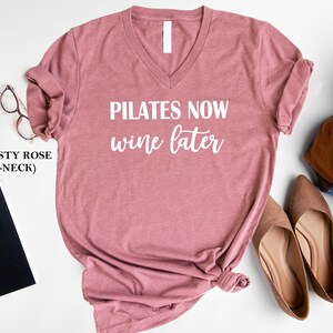K&ouml;nnte beinhalten: T-Shirt mit V-Ausschnitt in staubigem Rosa mit dem Text "Pilates Now Wine Later" in Wei&szlig;.