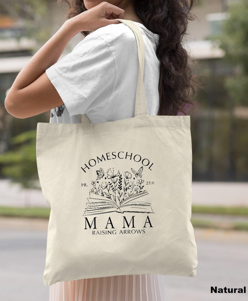 Peut inclure: Un sac fourre-tout en toile de couleur naturelle avec un motif graphique noir. Le motif pr&eacute;sente le mot "HOMESCHOOL" au-dessus d'un livre ouvert avec des fleurs et des papillons. En dessous, le mot "MAMA" est imprim&eacute;, suivi de "RAISING ARROWS".