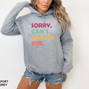 May include: A gray hooded sweatshirt with the text "SORRY. CAN'T. PILATES. BYE." printed in colorful letters.
