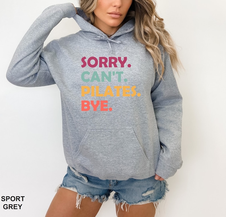 May include: A gray hooded sweatshirt with the text "SORRY. CAN'T. PILATES. BYE." printed in colorful letters.