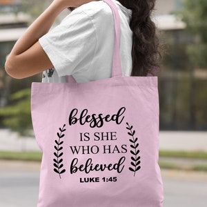 May include: Light pink tote bag with the text "blessed is she who has believed" and "LUKE 1:45" in black.