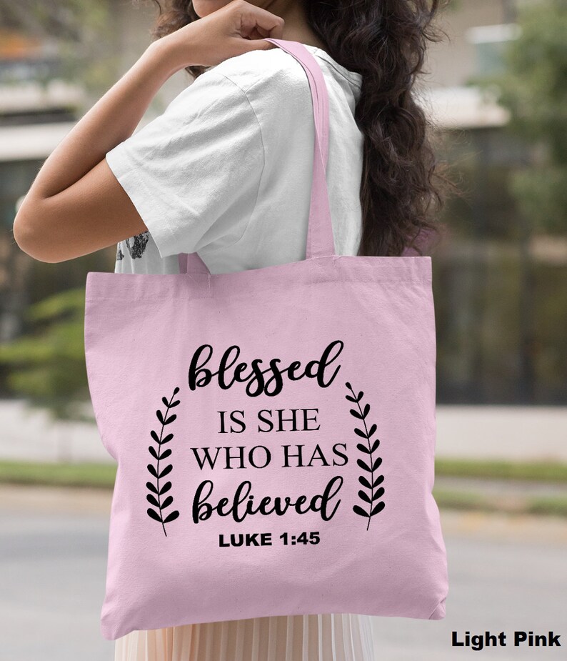 May include: Light pink tote bag with the text "blessed is she who has believed" and "LUKE 1:45" in black.