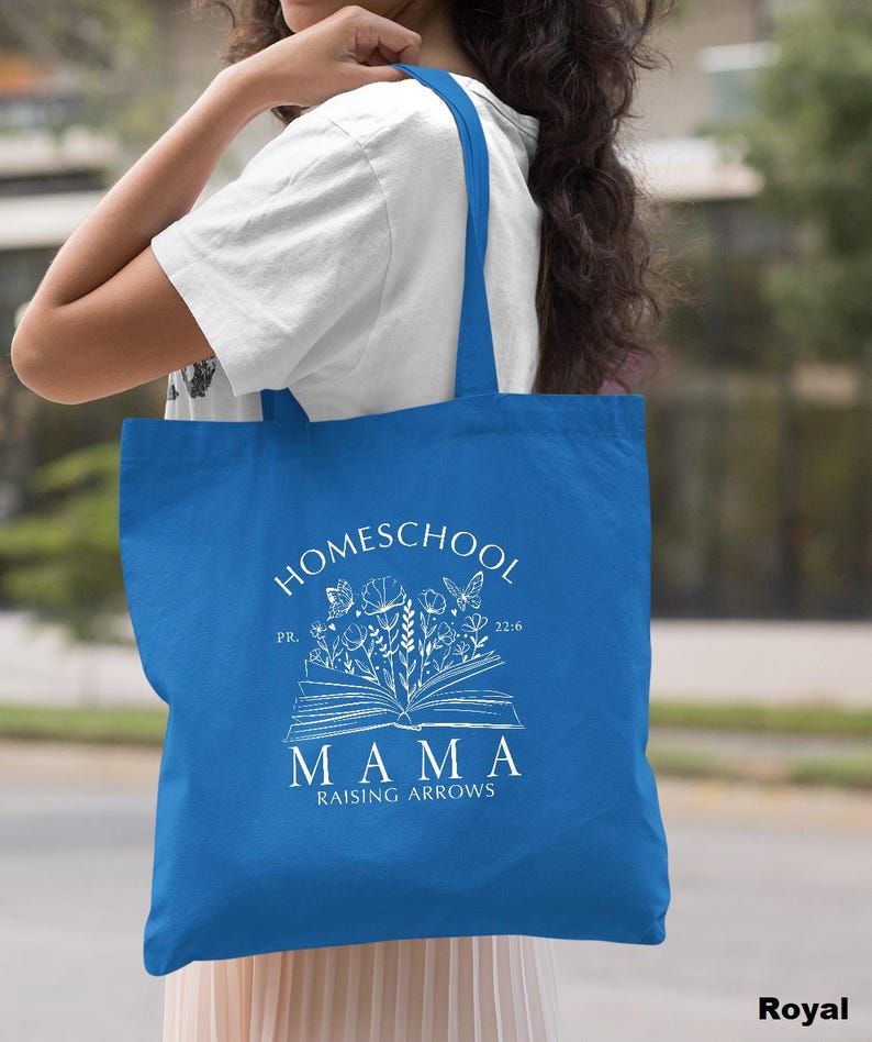 Peut inclure: Sac fourre-tout bleu roi avec texte blanc et illustrations florales. Le sac pr&eacute;sente les mots "Homeschool Mama Raising Arrows" avec un motif de livre ouvert et des graphiques de papillons et de fleurs. Le sac est port&eacute; &agrave; l'&eacute;paule.