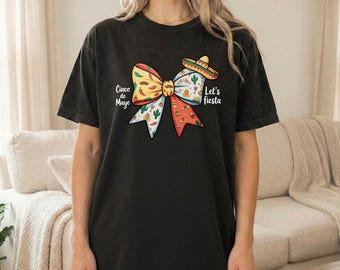May include: Black t-shirt featuring a colorful bow design with Cinco de Mayo and Let's Fiesta text. The bow includes patterns of cacti, mustaches, and a sombrero. The shirt is a casual, comfortable style.