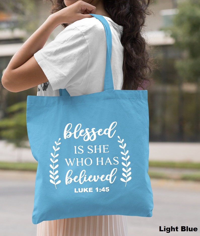 May include: Light blue tote bag with white text that reads "blessed is she who has believed" and "LUKE 1:45".