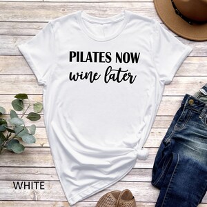 K&ouml;nnte beinhalten: Wei&szlig;es T-Shirt mit schwarzem Text, der "Pilates Now Wine Later" lautet.