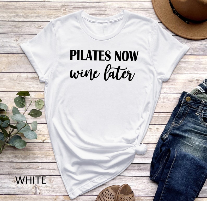 K&ouml;nnte beinhalten: Wei&szlig;es T-Shirt mit schwarzem Text, der "Pilates Now Wine Later" lautet.
