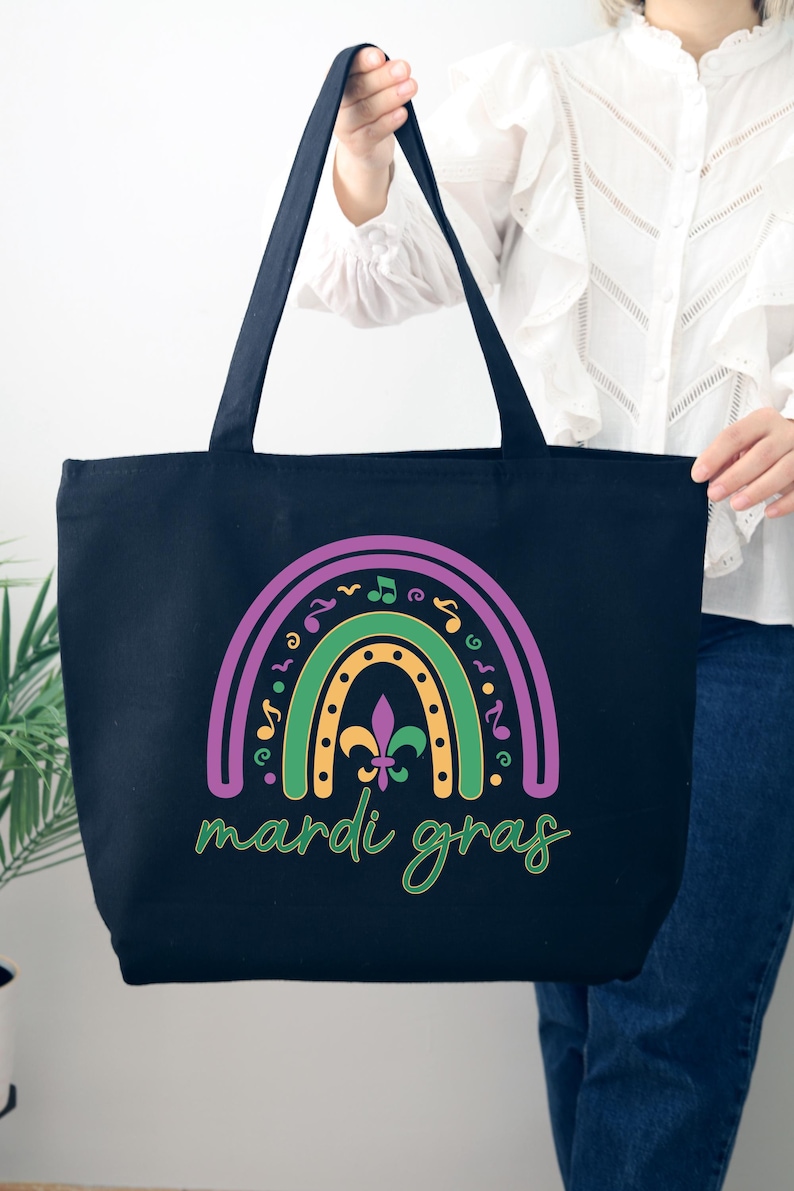 K&ouml;nnte beinhalten: Schwarze Tragetasche mit einem Regenbogen-Design in Lila, Gr&uuml;n und Gelb mit Noten und einer Fleur-de-lis. Der Text "Mardi Gras" ist in Gr&uuml;n unter dem Regenbogen geschrieben.