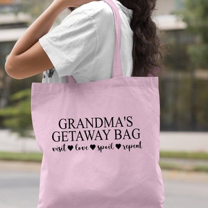 Pu&ograve; includere: Una borsa tote rosa chiaro con il testo "Grandma's Getaway Bag visit love spoil repeat" stampato in nero. La borsa ha manici neri.
