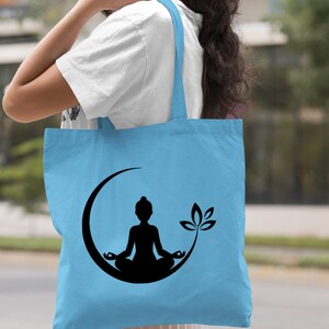 May include: Light blue tote bag with a black silhouette of a person meditating in a crescent moon with a lotus flower.