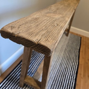 May include: A rustic wooden console table with a natural wood finish and a simple, rectangular design. The table has a distressed look and is supported by two sturdy legs.