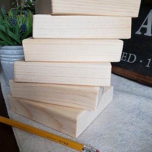 May include: A stack of five unfinished wooden squares, likely for crafts or DIY projects. The squares are arranged in a staggered pattern, with the top square slightly offset from the bottom square.