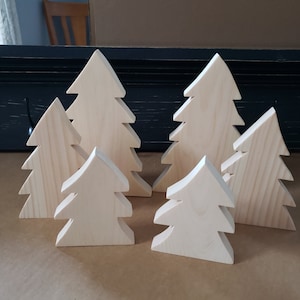 May include: Six wooden Christmas tree ornaments of varying sizes. The trees are all made of unfinished wood and have a simple, rustic design.