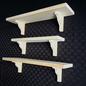 May include: Three wooden shelves with decorative corbel brackets. The shelves are made of natural wood and are unfinished.