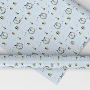 Puede incluir: Un papel de regalo azul y blanco con un diseño repetitivo de regaderas, flores y coronas. El papel está enrollado y listo para ser usado.