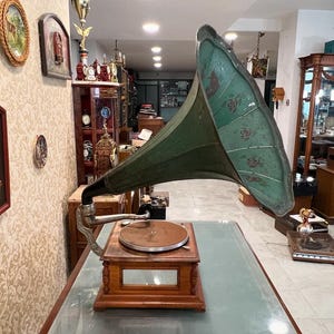 May include: A vintage green and gold gramophone with a large, decorative horn. The horn is painted with a floral design and has a green and gold finish. The gramophone is sitting on a wooden table.