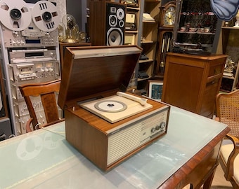 Puede incluir: Un tocadiscos vintage de madera con un gabinete de madera marrón y un plato giratorio blanco. El tocadiscos tiene una radio incorporada y una tapa deslizante.