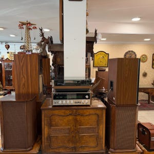 May include: A vintage stereo system featuring wooden speakers, a turntable, and a receiver. The speakers have a brown mesh front. The receiver has silver and black details. The system is on a wooden cabinet.