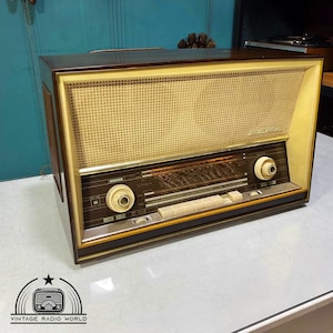 Könnte beinhalten: Ein vintage Radio in Braun und Creme mit einem Holzkasten und einer Metallfrontplatte. Das Radio hat ein Zifferblatt mit einem Zeiger und mehreren Knöpfen. Das Radio ist mit "SABA" beschriftet und hat ein Lautsprechergitter an der Vorderseite.