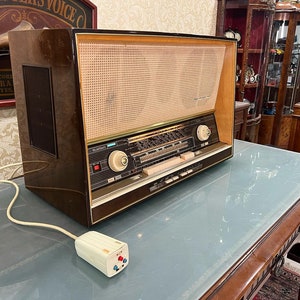Könnte beinhalten: Ein Vintage-Holzradio mit brauner und goldener Oberfläche. Das Radio hat einen großen Lautsprecher auf der linken Seite und ein Zifferblatt mit mehreren Knöpfen auf der rechten Seite. Das Radio steht auf einem Holztisch mit einer Glasplatte.