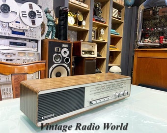 Puede incluir: Una radio vintage de madera con una rejilla de altavoz negra y botones plateados. La radio tiene un acabado de madera y el texto "Grundig" es visible en la parte delantera.